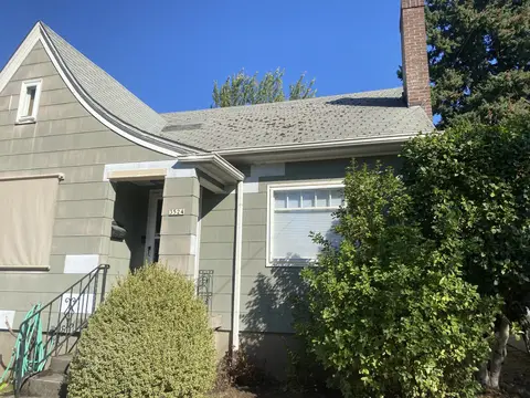 Single-story house with tan and white exterior siding, pitched roof, brick chimney, front entry with green railing, and