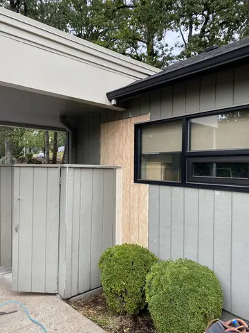 Modern house exterior with white and dark metal siding, black-trimmed windows, vertical wood accent panel, metal gate, and